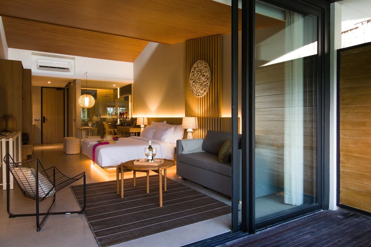 A modern hotel room with a bed, sofa, and a dining area.
