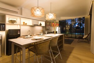Una cocina moderna con comedor, que incluye una isla grande, sillas de mimbre e iluminación colgante.