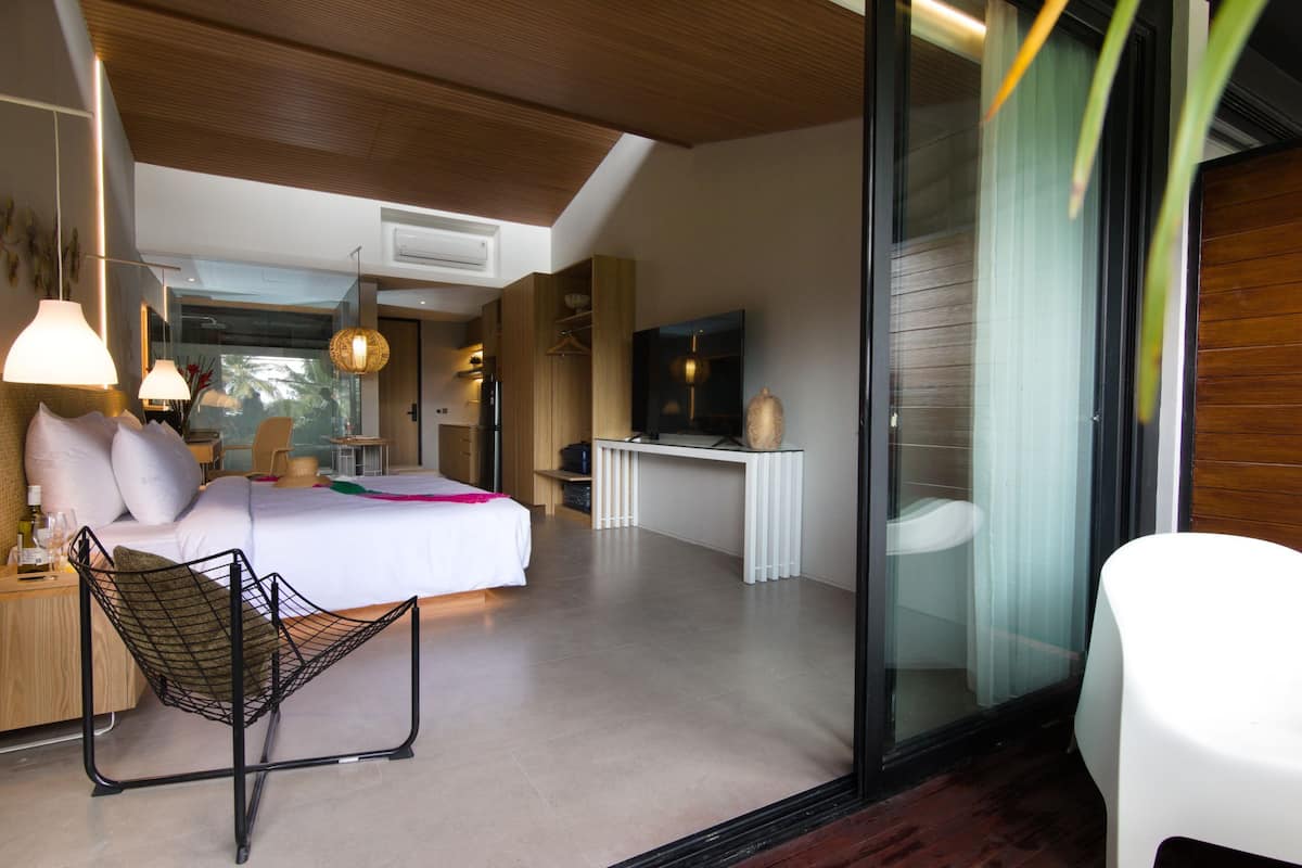 A modern bedroom with a bed, bedside table, chair, and a TV.