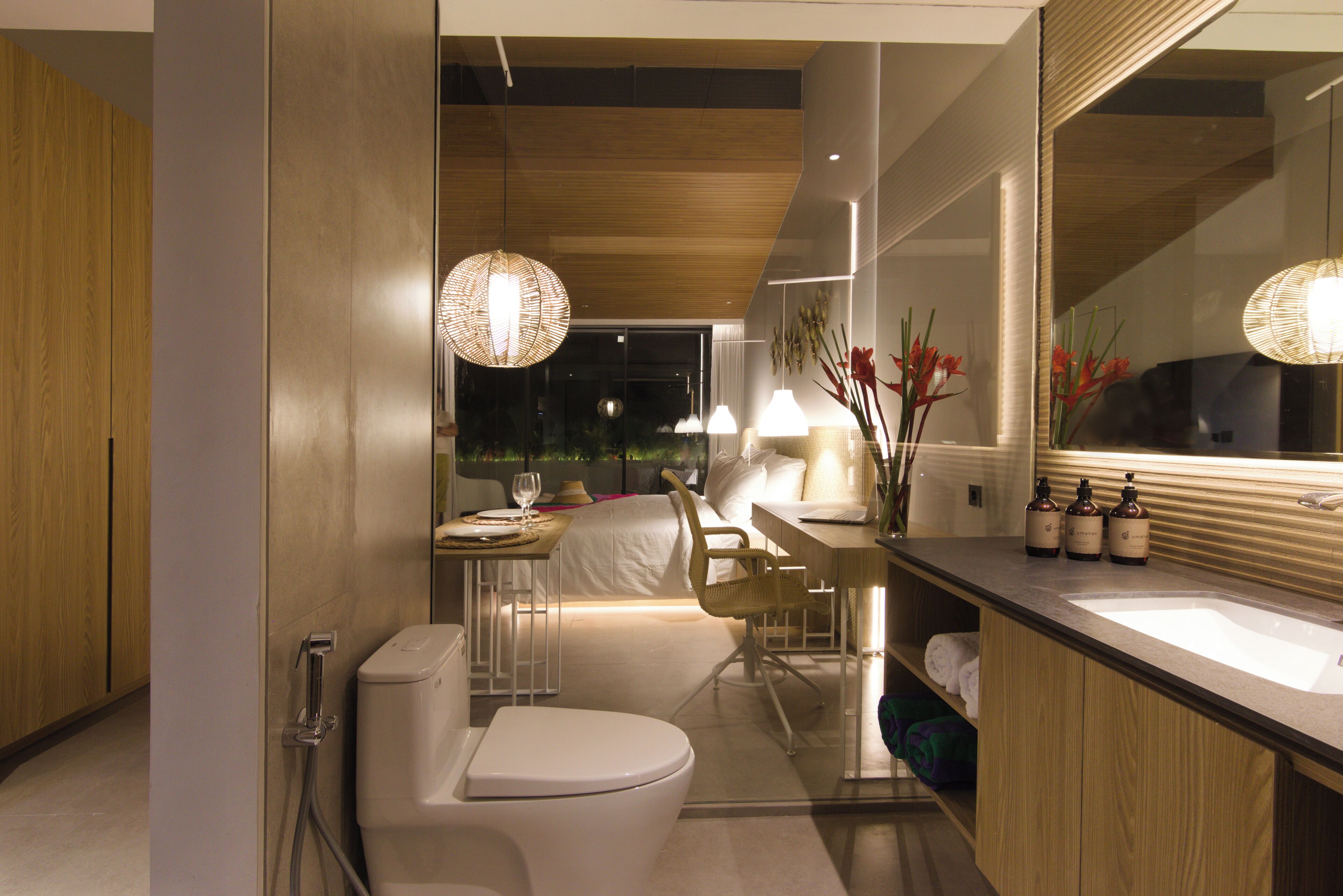 A modern bathroom with a toilet, sink, and shower. There is a small table with a chair and a lamp.