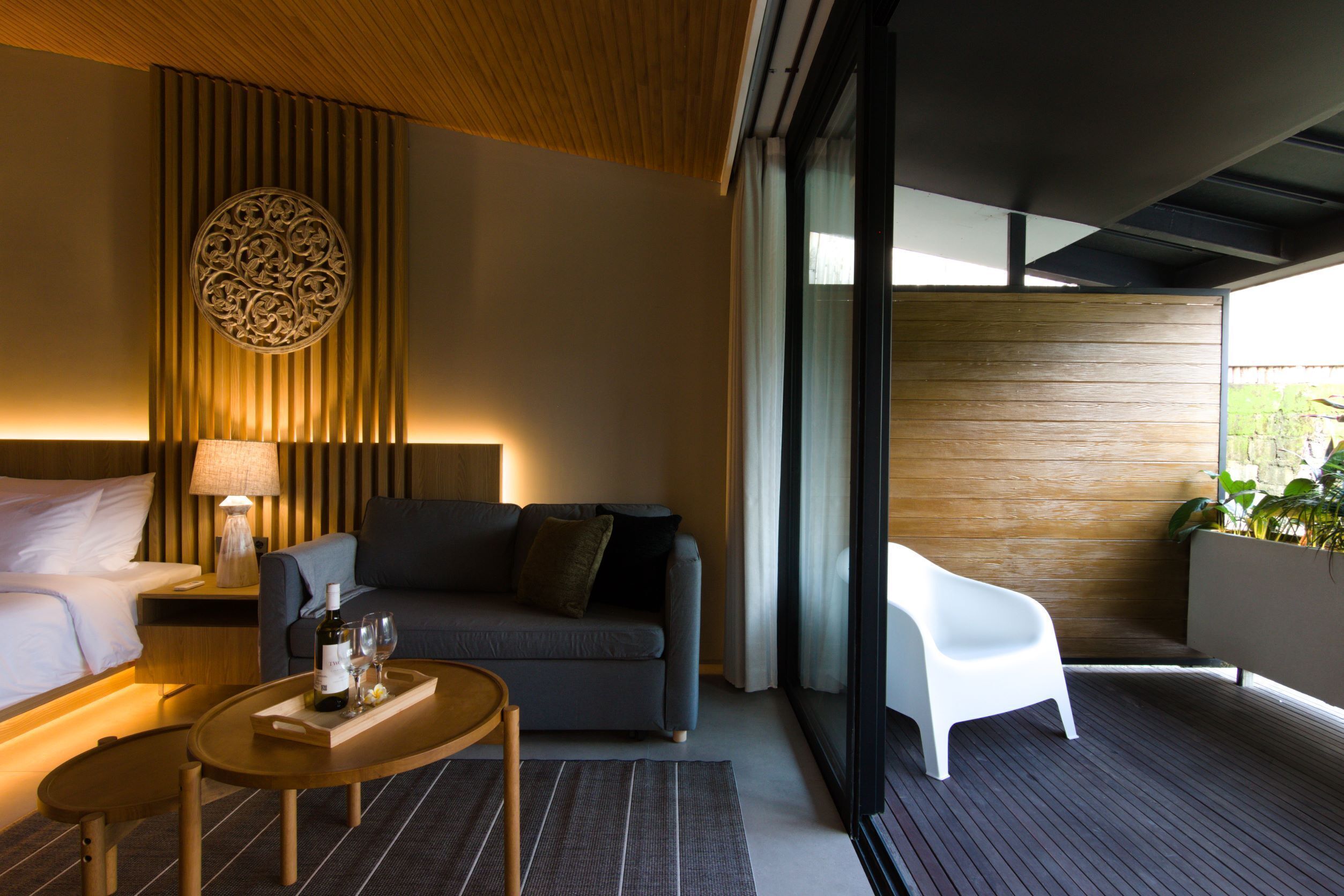 Een moderne hotelkamer met een bank, een klein tafeltje met dienblad, een lamp en uitzicht op groen door grote ramen.