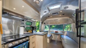 Une cuisine compacte pour camping-car, équipée d’une cuisinière, d’un évier et d’un coin repas avec une banquette.