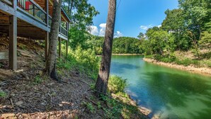 Une cabane en bois dotée d’une terrasse donnant sur une rivière, entourée d’une forêt dense.