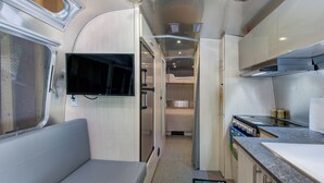 Une cuisine compacte équipée d’une cuisinière, d’un évier et d’un téléviseur à écran plat fixé au mur.