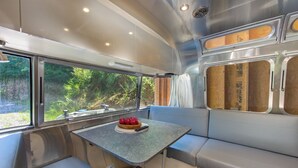 Un intérieur de camping-car moderne et compact, comprenant un coin repas, des sièges et de grandes fenêtres offrant une vue sur la verdure.