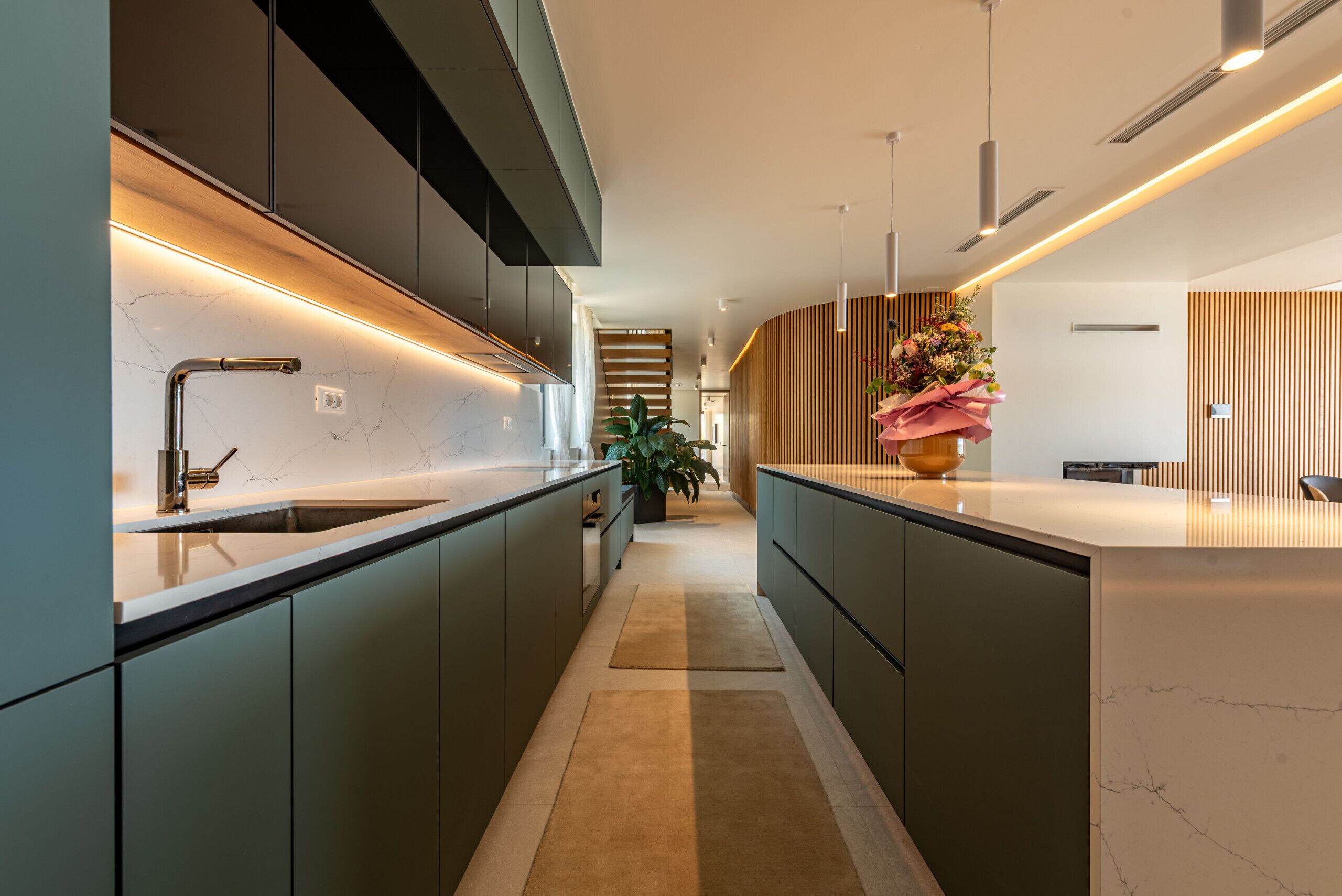 A modern kitchen with sleek cabinetry, a marble countertop, and a central island with a vase of flowers.