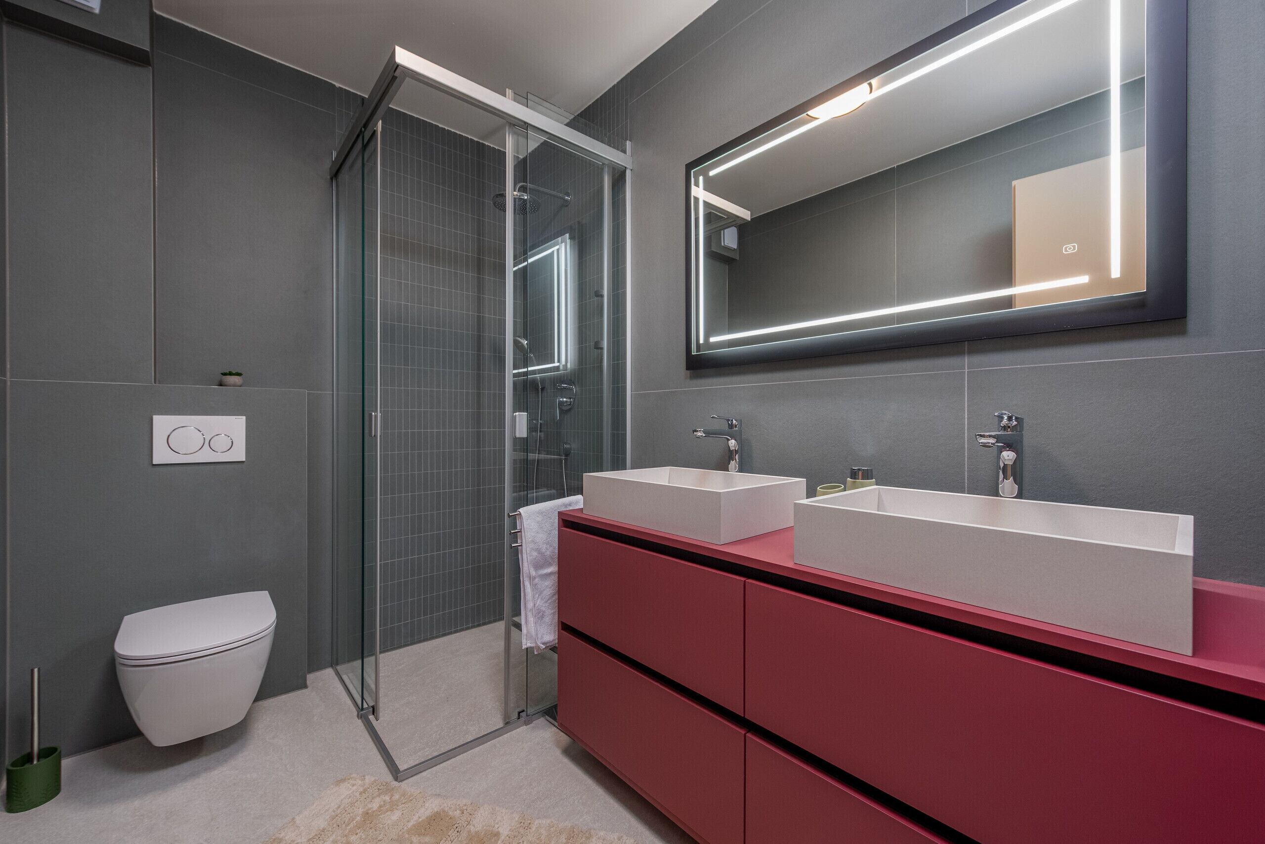 A modern bathroom with a glass shower enclosure, a white toilet, and a vanity with two sinks.