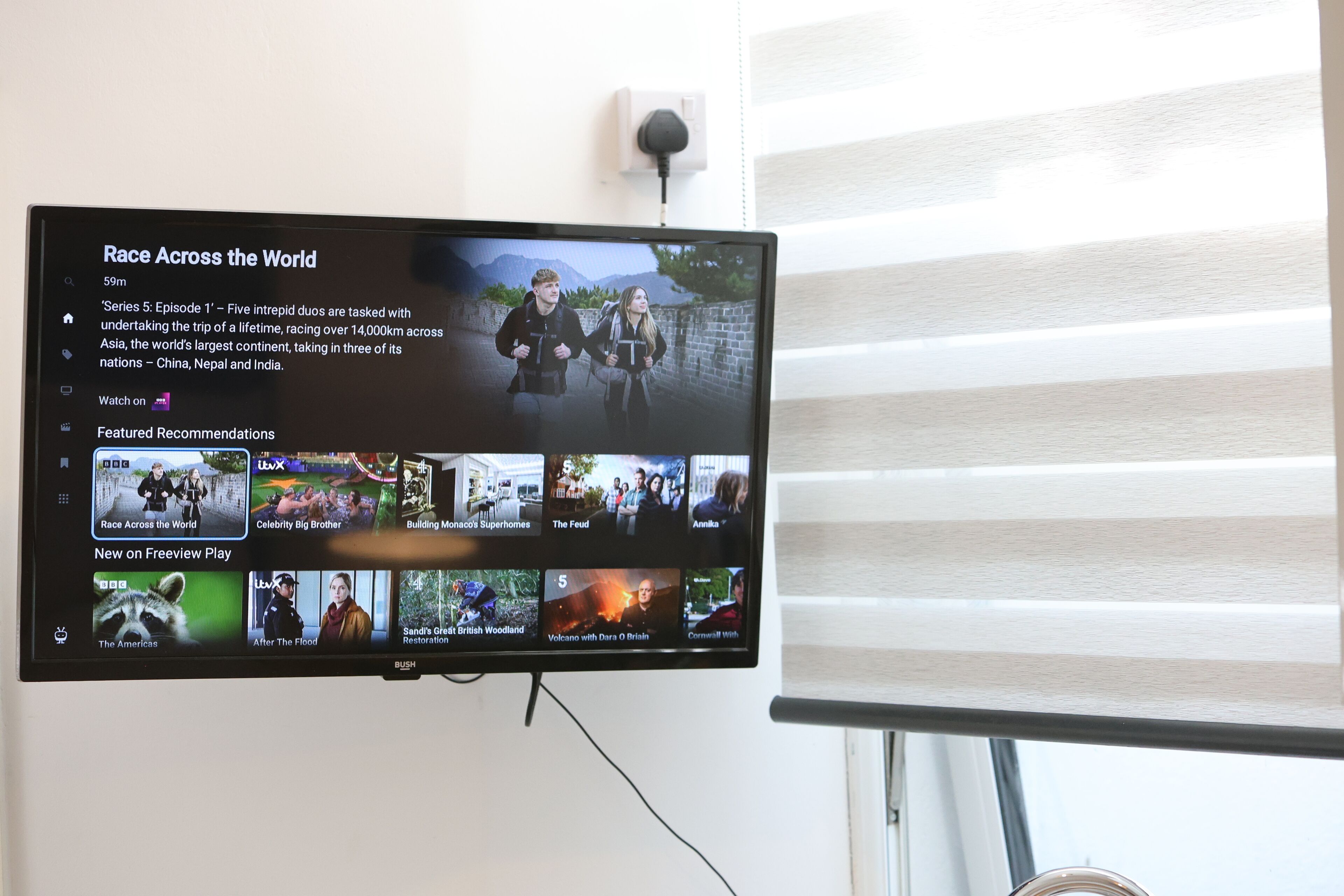 Ein an der Wand montierter Fernseher zeigt die Sendungsseite des Fernsehsenders mit verschiedenen Programmvorschlägen.