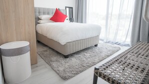 Quarto moderno com cama, tapete cinza, um banquinho de vime e parede cinza.
