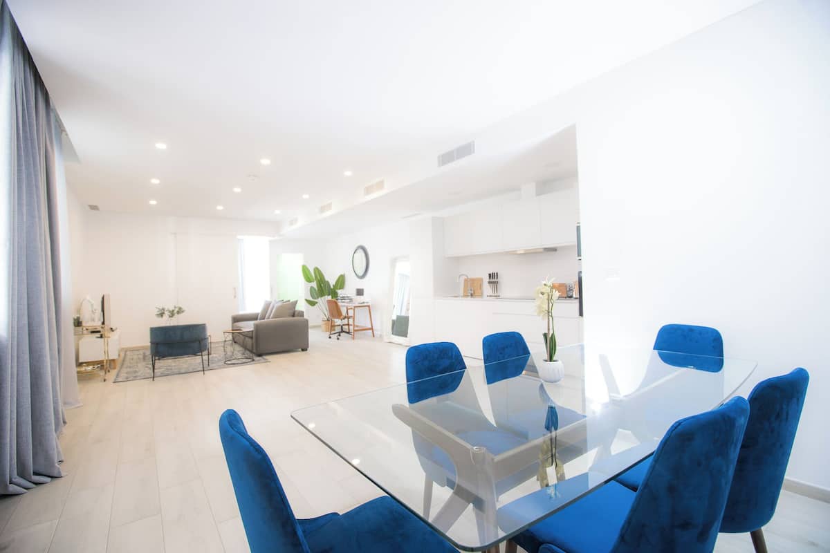 Un salón moderno con una mesa de comedor de cristal y sillas azules, un sofá y una mesa baja con una planta.