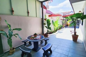 A covered outdoor area with a round table and benches, surrounded by potted plants and a view of neighboring buildings. - Ipoh Rainbow Blissful Home (Ipoh)