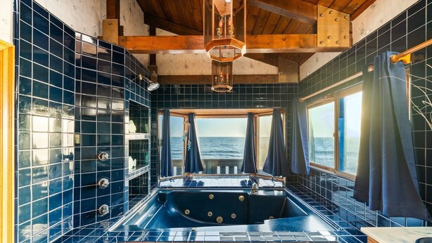 Un baño con una bañera grande, vigas de madera y vistas al mar.