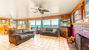 A spacious living room with a large window overlooking the ocean, a ceiling fan, and a fireplace. - 25% Off Aug WkDays On The Sand, Perfect 4 Families (Ventura)
