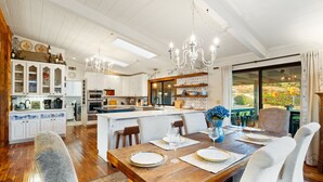 A spacious kitchen with white cabinetry, a central island, and a dining area with a wooden table set for six. - Perfect For Families, Near Wineries W/Private Pool (Temecula)