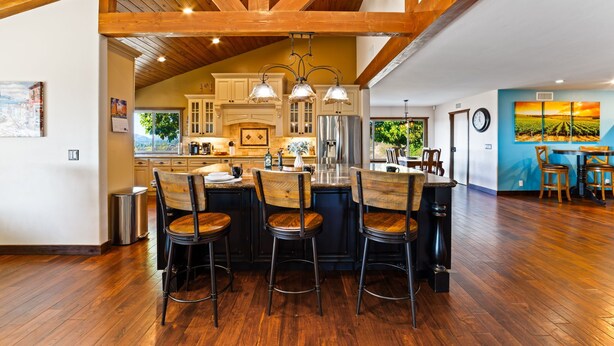 Une cuisine spacieuse avec des poutres en bois, un coin bar avec des tabourets et une table à manger avec des chaises.