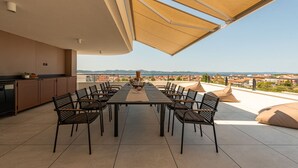 Uma área de refeições ao ar livre com mesa e cadeiras, cozinha e vista para a cidade.