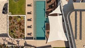 Vista aérea de um hotel moderno com piscina retangular, espreguiçadeiras e área de estar coberta.