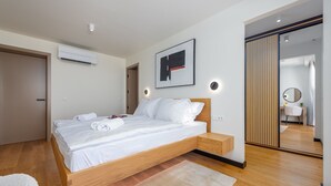 Quarto moderno com cama de madeira, roupa de cama branca, um espelho grande e uma porta de correr.