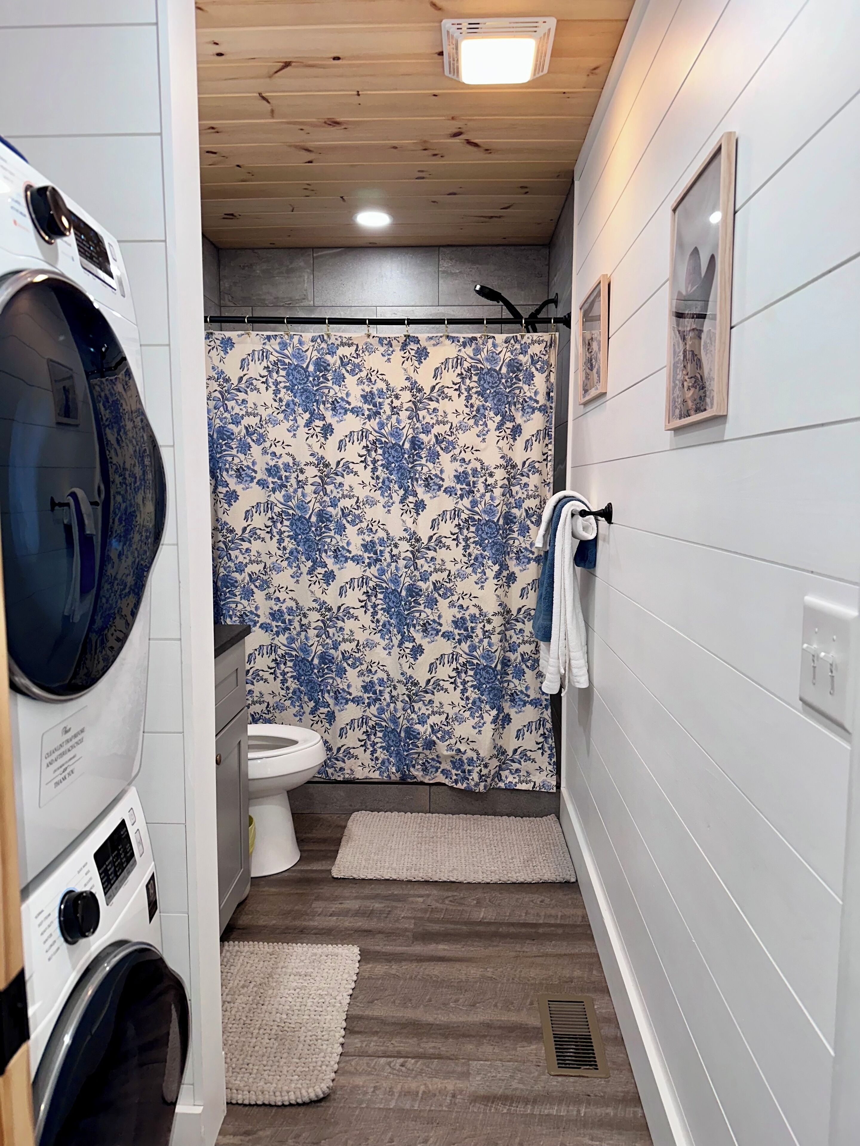 A compact laundry room with a washing machine, dryer, and a shower curtain with a floral pattern.