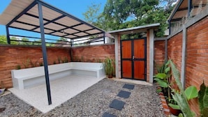 A covered outdoor area with a white bench, a door, and a brick wall. - Yustien Homestay Jogja 3 Bedroom - Entire House (Kasihan)