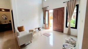A spacious living area with a high ceiling, a wooden door, and a view of the outdoors. - Yustien Homestay Jogja 3 Bedroom - Entire House (Kasihan)