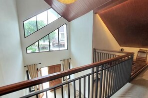 A high-ceilinged interior with a wooden railing, large windows, and a view of the outside. - Yustien Homestay Jogja 3 Bedroom - Entire House (Kasihan)
