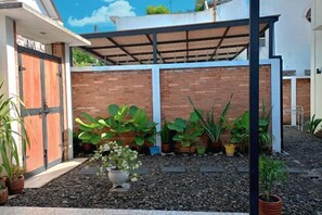 Une cour intérieure avec un mur en briques, des plantes en pot et une tonnelle en métal.