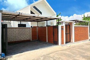 A gated entrance with a covered carport, a brick wall, and a white building with a sloped roof. - Yustien Homestay Jogja 3 Bedroom - Entire House (Kasihan)