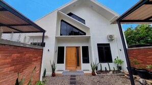 A modern two-story house with a wooden door, large windows, and a brick wall. - Yustien Homestay Jogja 3 Bedroom - Entire House (Kasihan)