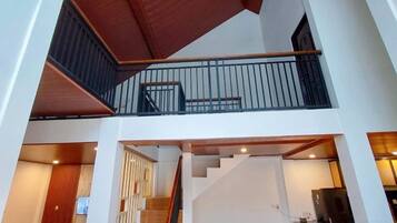 A multi-level interior with a staircase connecting two floors, a balcony with a railing, and a kitchen area with appliances.