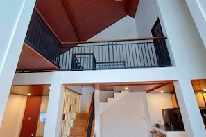 A multi-level interior with a staircase connecting two floors, a balcony with a railing, and a kitchen area with appliances. - Yustien Homestay Jogja 3 Bedroom - Entire House (Kasihan)