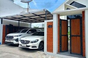 A modern house with a covered garage, two white cars parked inside, and a brick wall.