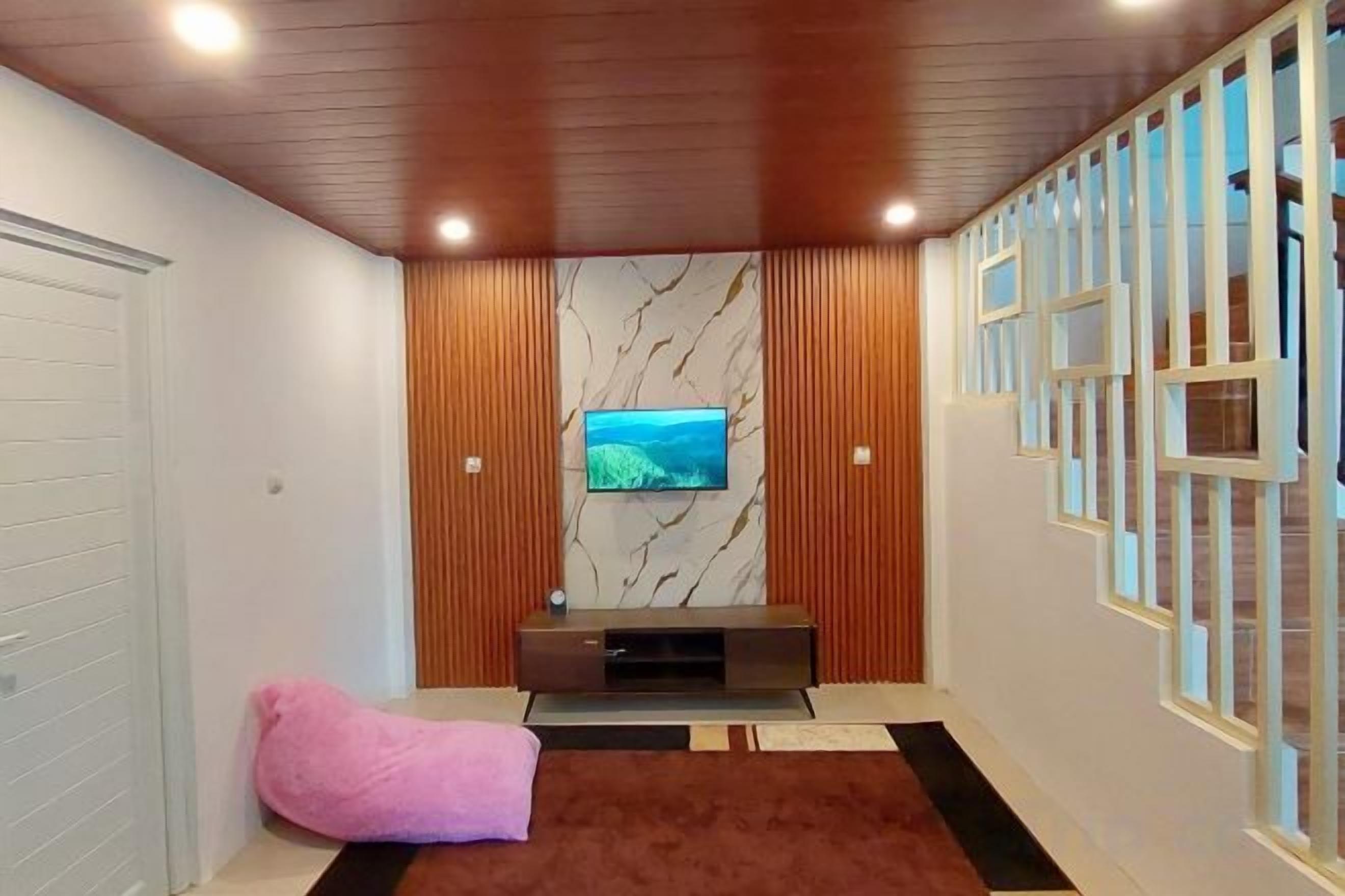 Una sala de estar moderna con televisor, paneles de madera, una pared de mármol y una alfombra estampada.
