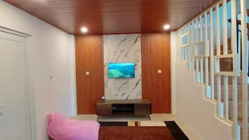 Una sala de estar moderna con televisor, paneles de madera, una pared de mármol y una alfombra estampada.