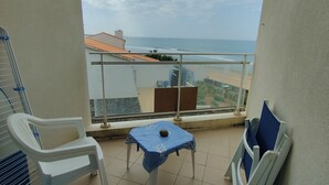 A balcony with a view of the sea, a table, and two chairs.