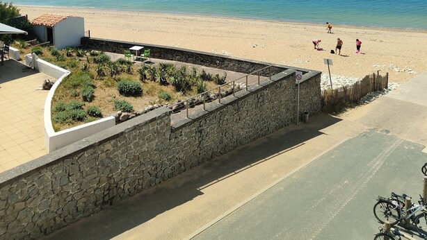 A beach view with a stone wall, a patio area, and a clear blue sky.