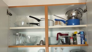 A kitchen with a wooden cabinet containing various kitchenware, including pots, pans, and glassware.