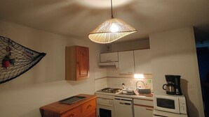 A compact kitchen with a stove, microwave, and coffee maker. There is a wooden cabinet and a hanging light fixture.
