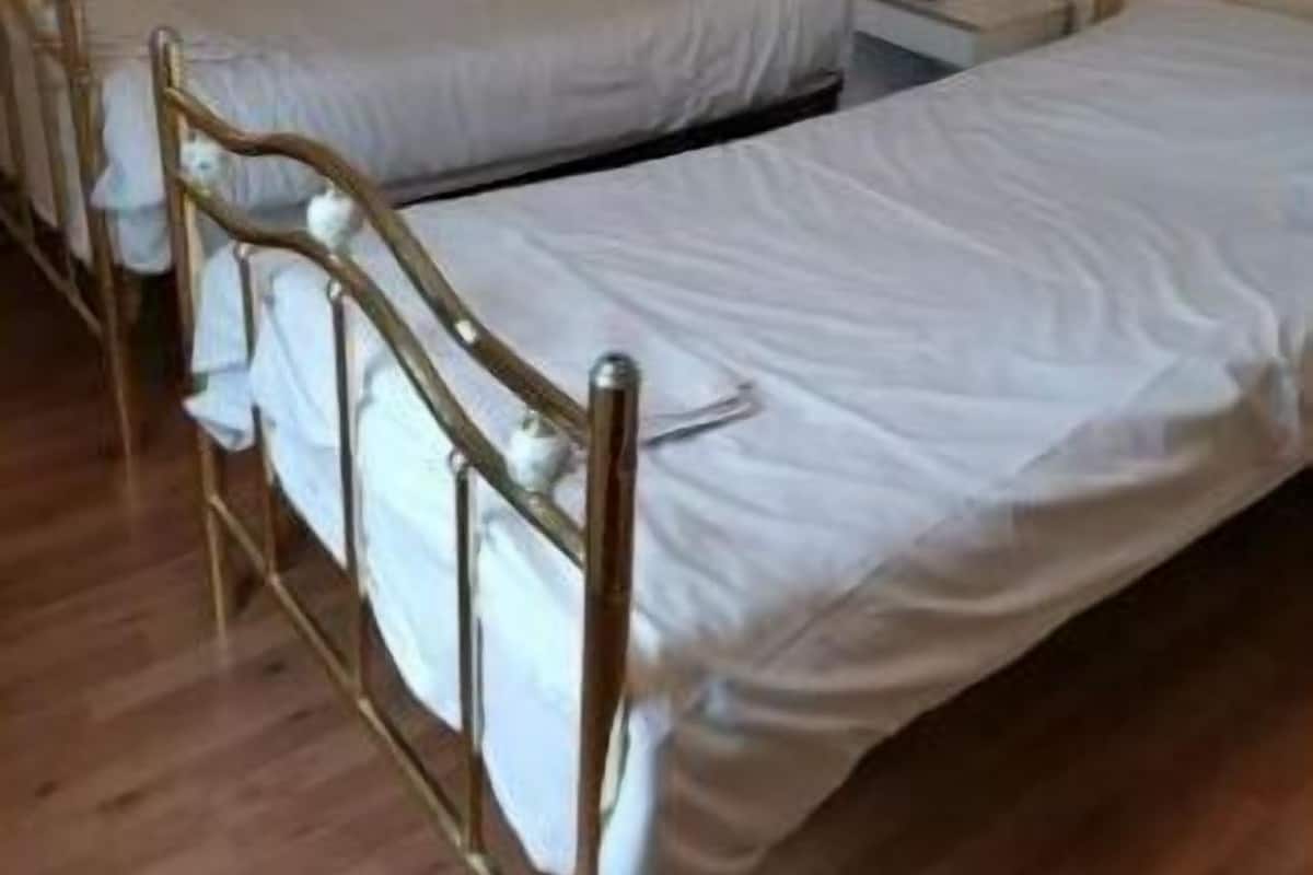 Quarto com duas camas de solteiro, cabeceiras de madeira e mesa de cabeceira com abajur.