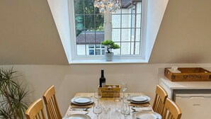 A dining area with a wooden table set for six, surrounded by wooden chairs. A chandelier hangs above, and a potted plant is on the windowsill. - Modern Studio in Chandlers Ford (Chandler's Ford)
