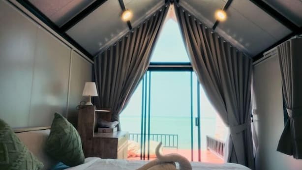 A bedroom with a bed, pillows, a nightstand, a lamp, and a view of the sea through a large window. - Jayden Villas (Koh Phangan)