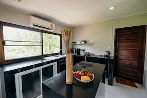A modern kitchen with a window, a dining table, and a vase with dried plants. - Jayden Villas (Koh Phangan)
