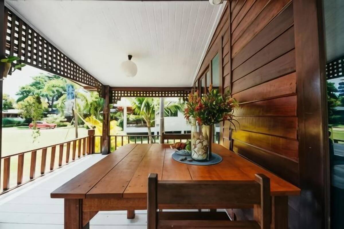 A wooden table with chairs, a potted plant, and a view of a garden.