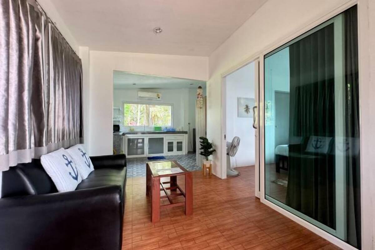 A living room with a sofa, a wooden coffee table, and a sliding glass door leading to a kitchen and dining area.