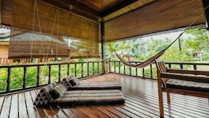 A wooden deck with a hammock, cushioned seating, and a view of greenery. - Jayden Villas (Koh Phangan)