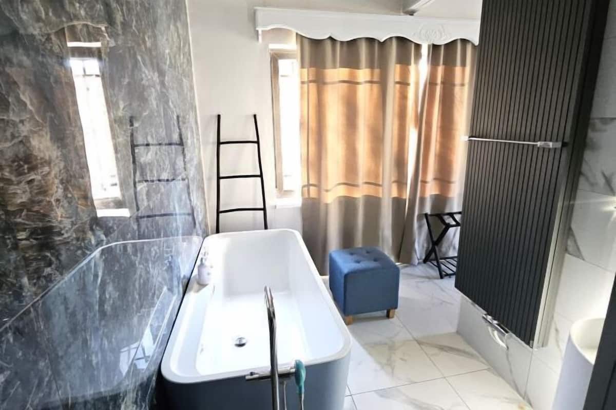 A bathroom with a bathtub, a towel rack, a window with curtains, and a tiled floor.
