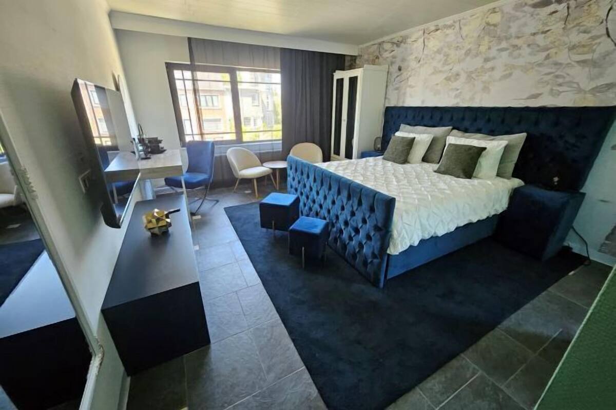 A bedroom with a large bed, a desk, a chair, and a TV.