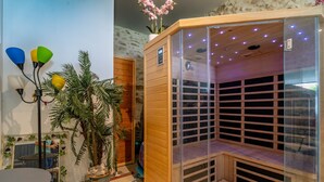 A sauna with wooden slats and a glass enclosure, a potted plant, and a table with chairs.