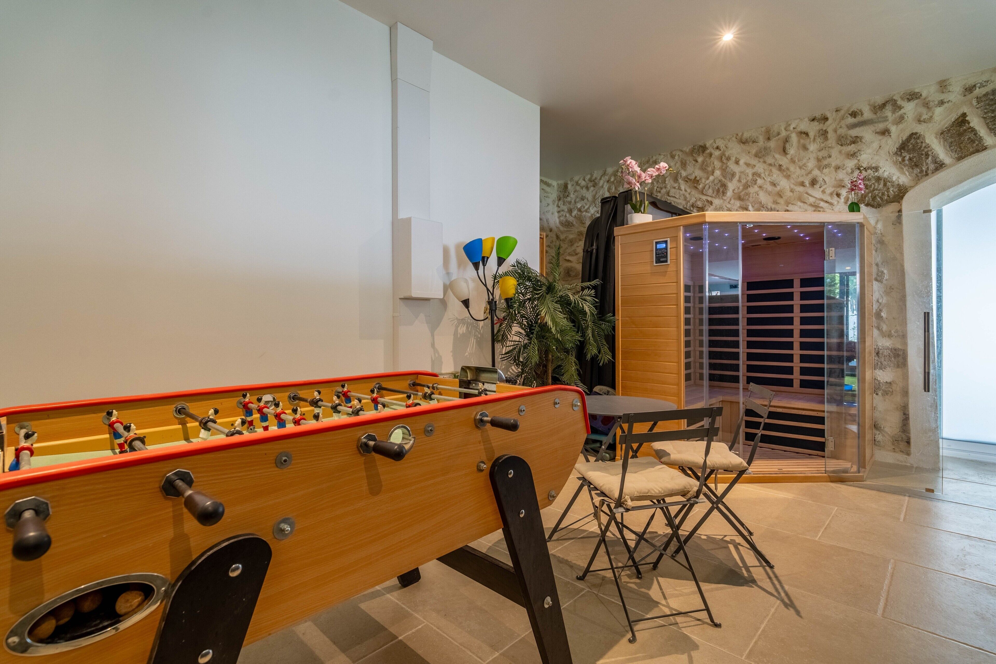 A foosball table, a folding chair, and a wooden cabinet with a glass door in a room with stone walls and a tiled floor.
