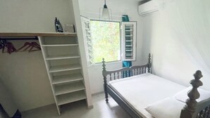 Et soveværelse med en seng, et skab, et vindue med gardiner og en hængende lampe.
